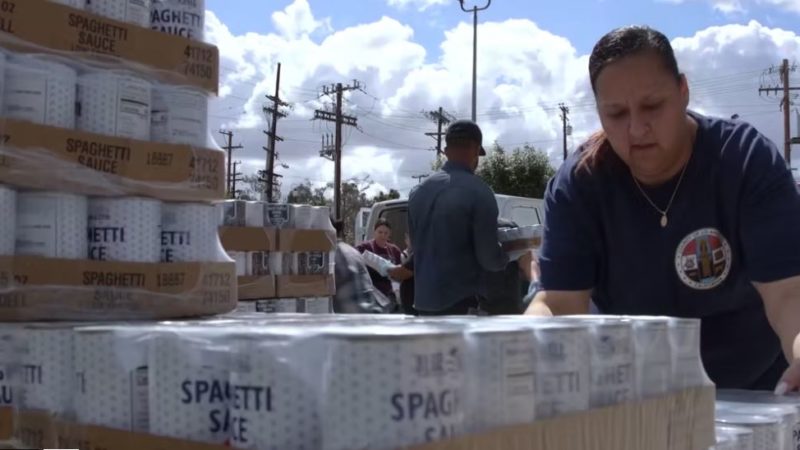 An LA County disaster service worker moves boxes of food at a distribution event.