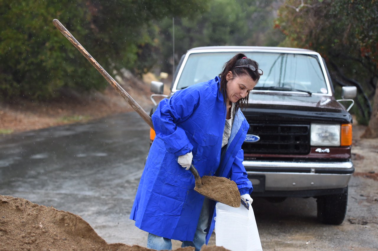 A resident scoops sand into a sandbag during a rainstorm.