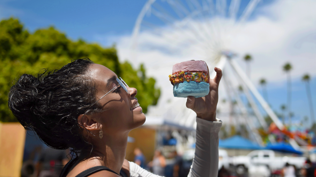 An LA County Fair attendee holds up a dessert in front of the ferris wheel.