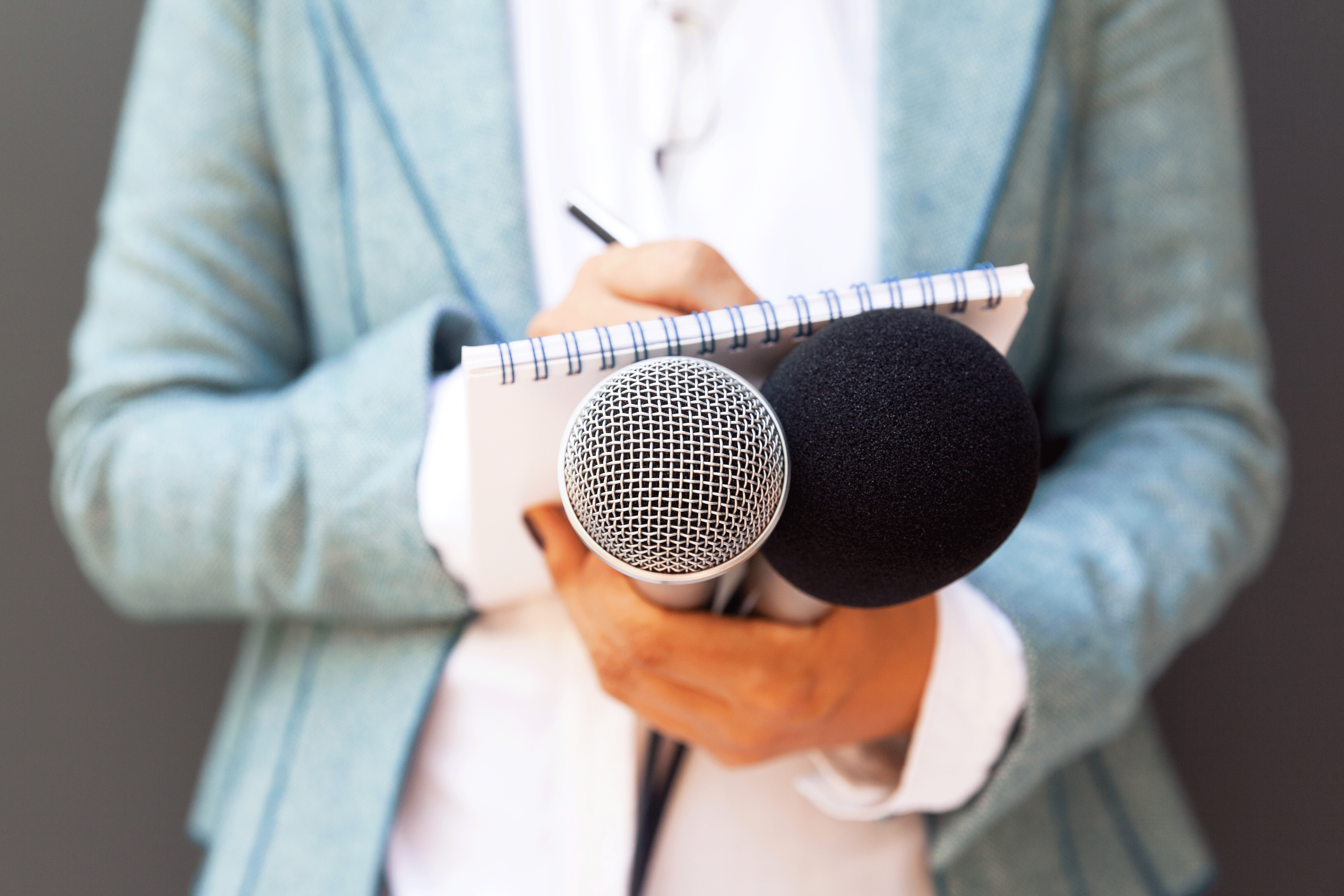A person holds a microphone and takes notes.