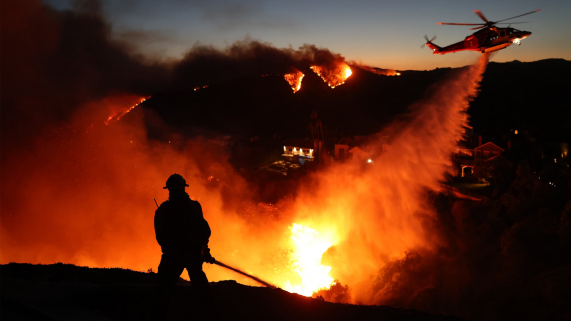 A firefighter battles a local widlfire overnight. A helicopter drops aerial resources in the background.