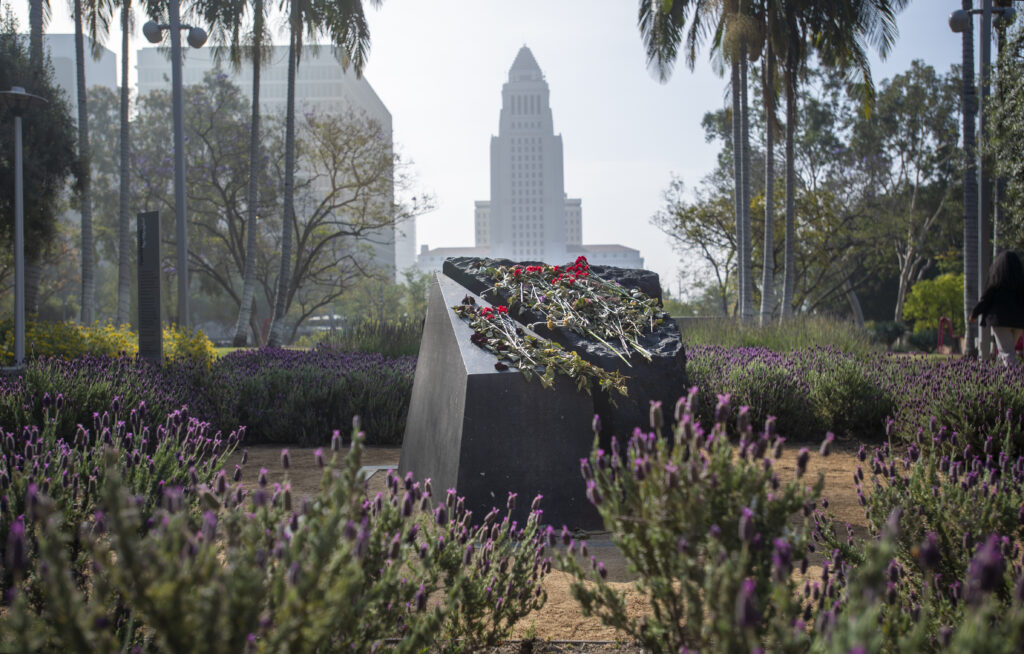 Armenia Genocide Memorial with flowers on top of it in Gloria Molina Grand Park with white Los Angeles City Hall building in the background