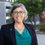 Maral_Karacussian_2025 Woman wearing glasses, heart shape necklace, black dress jacket and green blouse